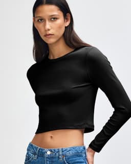 A black long-sleeve cropped fitted T-shirt on a model, featuring a logo. The shirt has a tight, sleek fit.