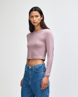 A fitted long-sleeve crop T-shirt in a soft lavender colour, worn by a model with straight hair, paired with blue jeans.