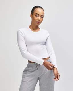 A fitted white long-sleeve cropped T-shirt worn with grey sweatpants, featuring a logo on the shirt.