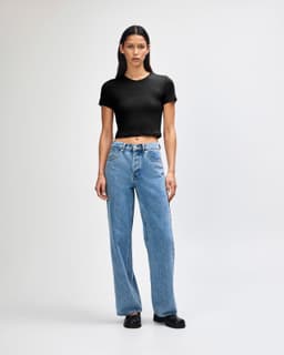 A black crop fitted T-shirt paired with light blue wide-leg jeans, displayed on a model against a plain background.