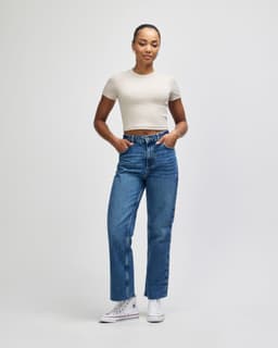 A fitted cream crop t-shirt paired with blue jeans, worn by a woman standing with hands on hips.