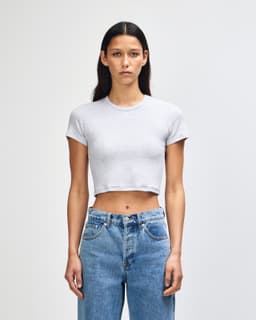 A grey women's crop fitted T-shirt with short sleeves, paired with high-waisted denim jeans, featuring a logo.