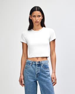 A white women's crop fitted T-shirt paired with blue high-waisted jeans, featuring a simple design and a logo.