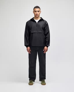 A black packable anorak jacket worn by a model, paired with dark trousers and shoes, featuring a logo.
