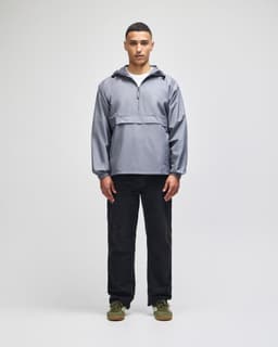 A packable anorak jacket in grey, featuring a half-zip closure and a logo, displayed by a model wearing black pants.