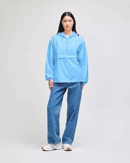 A packable anorak jacket in light blue, featuring a hood and a front pocket, worn with denim jeans.