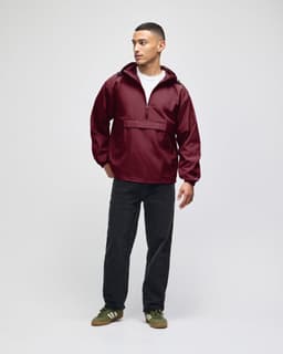 A maroon packable anorak jacket with a hood, worn by a model, paired with dark pants and green shoes.