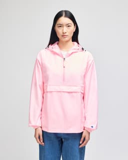 A pink Champion Adult Packable Anorak Jacket featuring a hood and a front pocket, worn by a model.