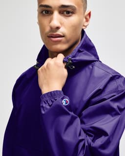 A purple packable anorak jacket with a logo, featuring a high collar and adjustable drawstring.