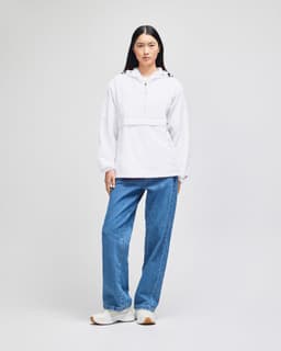 A woman wearing a white Champion Adult Packable Anorak Jacket paired with blue jeans and white sneakers, standing against a light background.