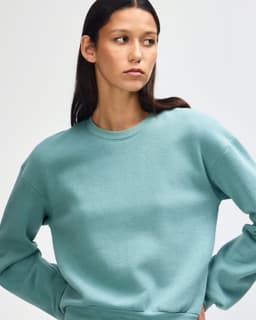 A teal women's crewneck sweatshirt made from fleece, featuring a simple design and a logo.