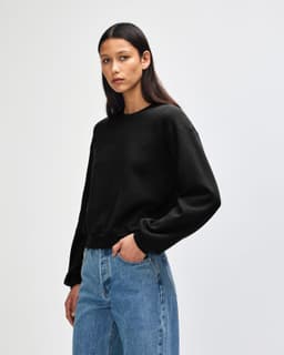 A women's black crewneck sweatshirt displayed on a model, featuring long sleeves and a relaxed fit.