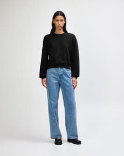 A black crewneck sweatshirt paired with light blue wide-leg jeans on a model. The sweatshirt has a logo.