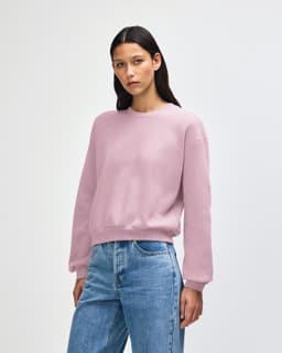 A woman wearing a pink American Apparel Reflex Fleece women's crewneck sweatshirt paired with blue jeans.