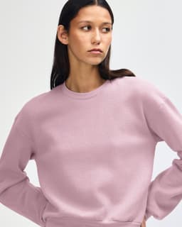 A women's crewneck sweatshirt in a soft pink hue. It features a relaxed fit and has a logo.