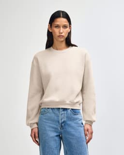 A women's crewneck sweatshirt in a beige colour, featuring a relaxed fit and long sleeves. It has a simple logo.
