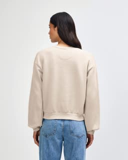 A women's crewneck sweatshirt in a light beige colour, featuring a relaxed fit and long sleeves. It has a logo.
