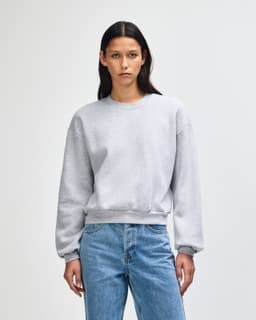 A grey women's crewneck sweatshirt with a relaxed fit and long sleeves, featuring a small logo.
