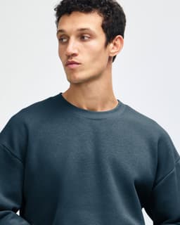 A unisex crewneck sweatshirt in deep teal, featuring long sleeves and a relaxed fit, with a logo present.