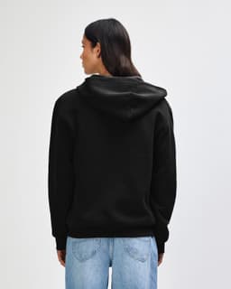 A model wearing a black unisex full zip hooded sweatshirt paired with light blue baggy jeans and black sneakers.