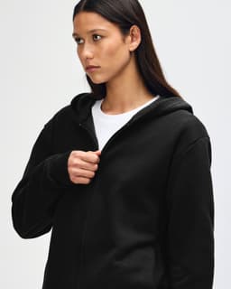 A black unisex full zip hooded sweatshirt features a hood and a front zip, displayed on a model.