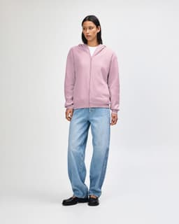 A unisex full zip hooded sweatshirt in soft pink, featuring a relaxed fit and a front zip. It has a logo.