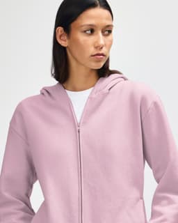 A unisex full zip hooded sweatshirt in a soft pink colour, featuring a hood and a brand logo.