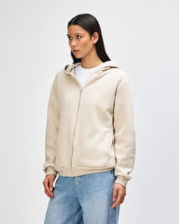 A unisex full zip hooded sweatshirt in a light beige colour, featuring a hood and a zip closure, shown on a model.