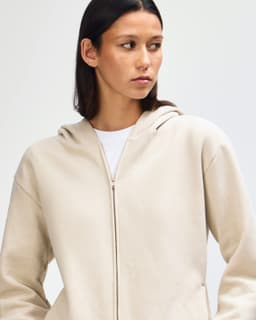 A unisex full zip hooded sweatshirt in a light cream colour, featuring a hood and front zipper.