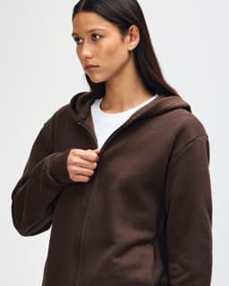 A brown unisex full zip hooded sweatshirt displayed on a model with curly hair. The sweatshirt has a logo.