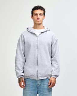 A unisex full zip hooded sweatshirt in heather grey with a hood and pockets. The model stands with hands in pockets.
