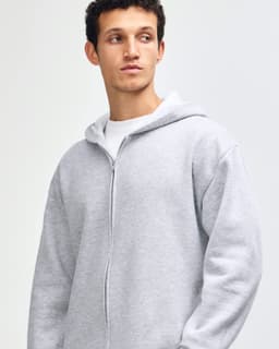 A unisex full zip hooded sweatshirt in grey, featuring a logo and paired with light blue jeans.