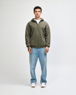 A model wearing an olive green unisex full zip hooded sweatshirt paired with light blue oversized jeans.