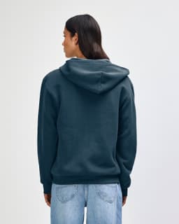 A navy blue unisex full zip hooded sweatshirt, featuring a hood and a logo. The model has curly hair and faces away.