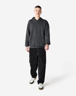 A unisex hooded sweatshirt in dark grey, worn by a model with baggy black trousers and white sneaker accents.