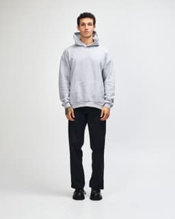 A unisex grey hooded sweatshirt with a kangaroo pocket, paired with light blue jeans and black sneakers.