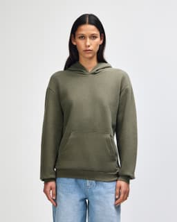 A unisex hooded sweatshirt in olive green with a front pocket and a logo, modelled by a male figure.