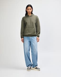 A model wearing an olive green unisex hooded sweatshirt, paired with black cargo pants and sneakers.