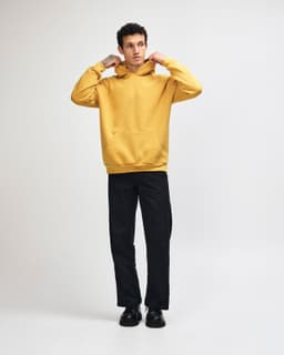 A unisex hooded sweatshirt in mustard yellow with a front pocket and a relaxed fit, featuring a logo.