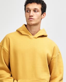 A unisex hooded sweatshirt in a warm gold colour, featuring a front pocket and a relaxed fit. It has a logo.