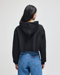 A black cropped hoodie with a hood, worn by a person facing away, paired with blue jeans.
