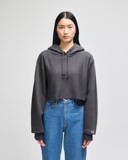 A grey cropped hoodie with a hood and long sleeves, featuring a small logo on the cuff.