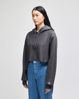 A cropped hoodie in dark grey, featuring a hood and long sleeves, with a small logo on the sleeve.