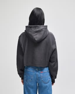 A cropped black hoodie with a hood, seen from the back, paired with blue jeans. It features a logo on the garment.