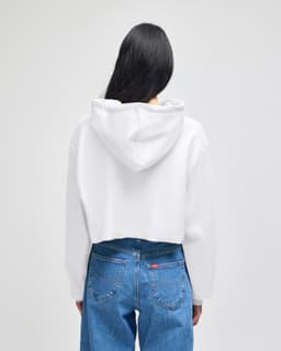 A white cropped hoodie with a hood, displayed from the back, paired with blue jeans. It features a logo.
