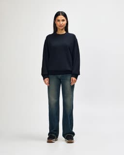 A young man wearing a black Gildan Softstyle adult sweatshirt, paired with black jeans and sneakers.