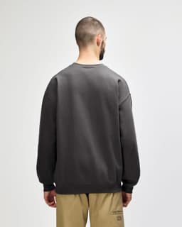 A back view of a woman wearing an olive green Gildan Softstyle adult sweatshirt with a logo.