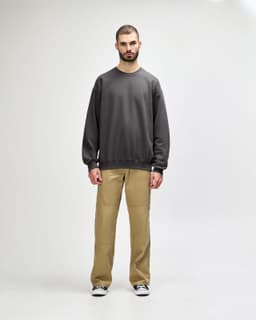 A woman wearing a dark green sweatshirt paired with blue jeans and white sneakers, standing casually.