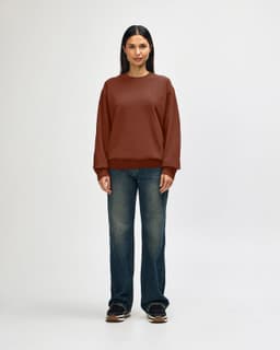 A brown Gildan Softstyle adult sweatshirt is worn by a model, paired with black pants and sneakers.