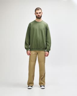 A green Gildan Softstyle adult sweatshirt worn by a model, paired with dark pants and black sneakers.